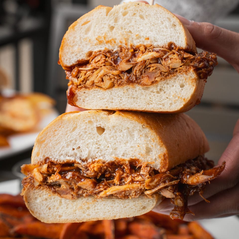 Two stacked sandwiches filled with saucy shredded meat on soft white bread, held in hands.