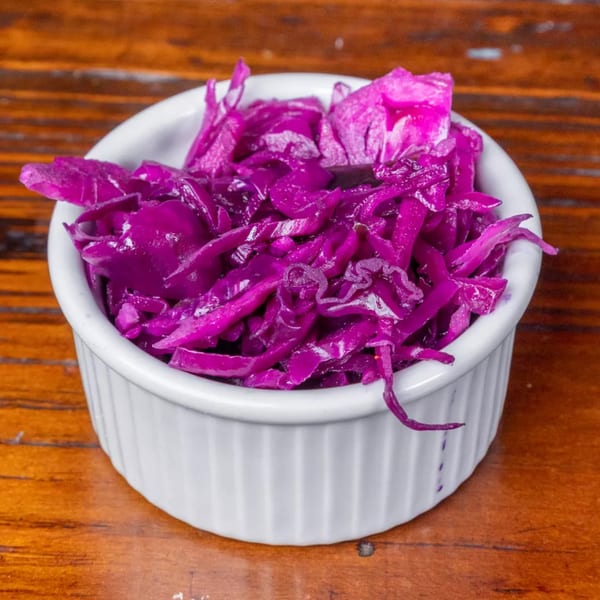 Close-up of vibrant purple pickled cabbage in a white ramekin on a wooden table.