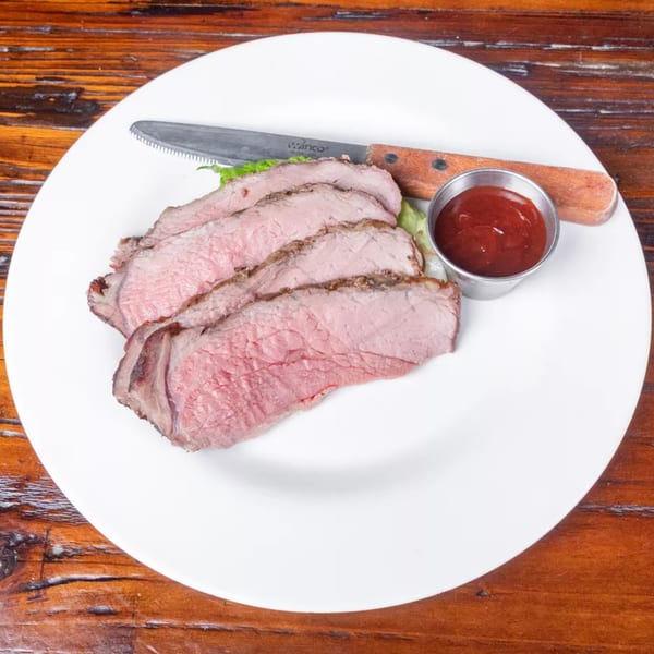 Slices of medium-rare roast beef with a side of ketchup and a steak knife on a white plate.