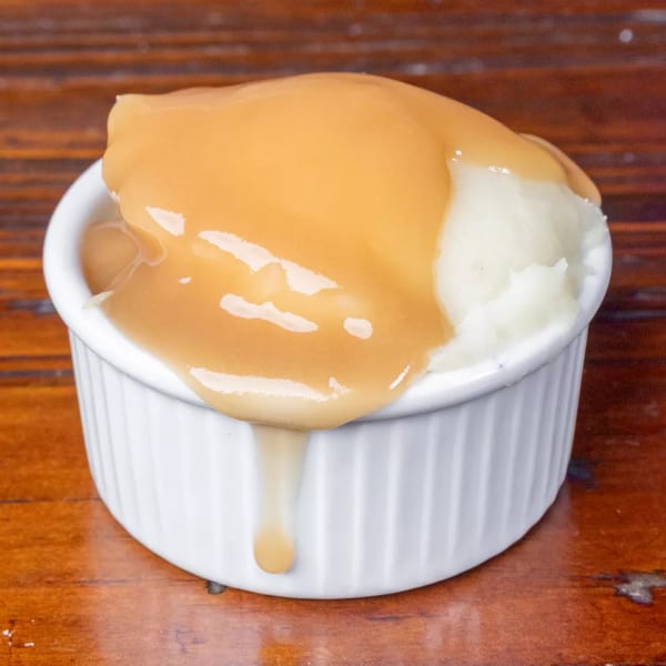 Creamy mashed potatoes topped with rich brown gravy, served in a white ramekin on a wooden table.