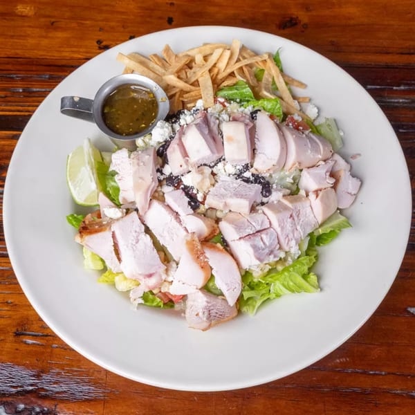 A chicken salad with lettuce, black beans, corn, cheese, tortilla strips, lime, and dressing.