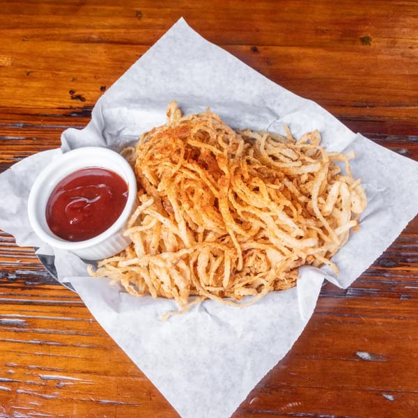 Crispy fried onion strings with seasoning, served in a basket with a side of ketchup.