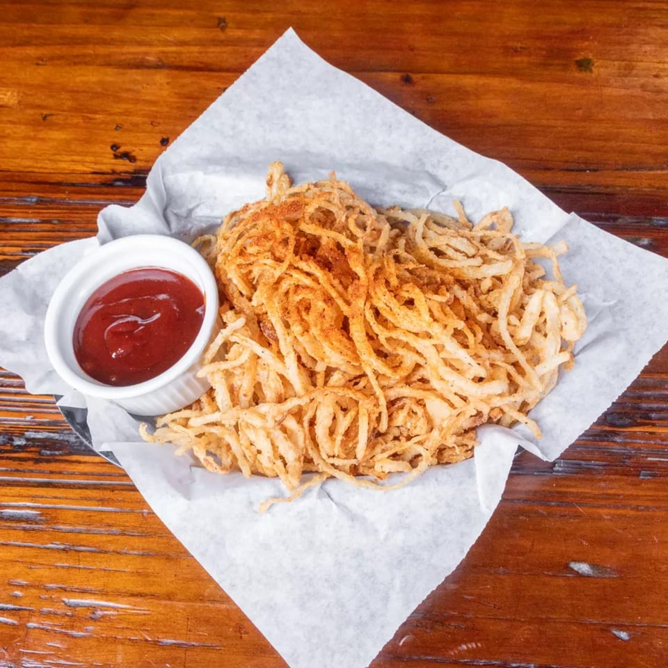 Crispy fried onion strings with seasoning, served in a basket with a side of ketchup.