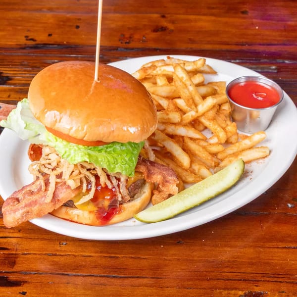 A bacon cheeseburger with lettuce, tomato, crispy onions, fries, ketchup, and a pickle spear.