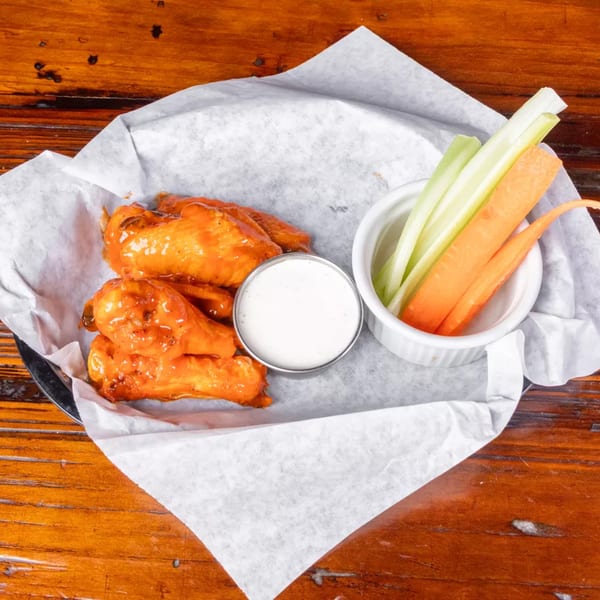 Buffalo wings with ranch dressing, celery, and carrots in a paper-lined basket on a wooden table.