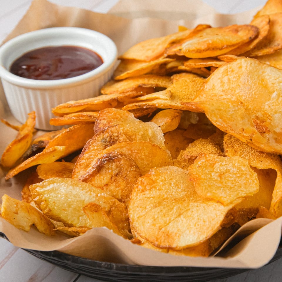 Pile of golden fried tortilla chips served with a small bowl of dark dipping sauce on a paper-lined plate.